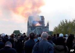 People watch as flames and smoke rise from Notre Dame cathedral as it burns in Paris, Monday, April 15, 2019.
