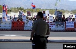 A police officer looks on as protesters line one side of a roadway leading to Sunnylands where U.S. President Obama prepares to host leaders from Southeast Asia at the ASEAN Summit in Rancho Mirage, California, Feb. 15, 2016.