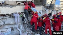 Rescuers carry a woman after she was evacuated from under a collapsed building following an earthquake in Kahramanmaras