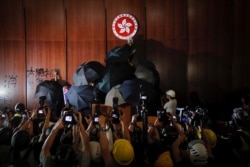 FILE - Journalists film a protester defaceing the Hong Kong emblem inside the meeting hall of the Legislative Council in Hong Kong, July 1, 2019.