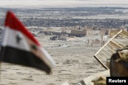 FILE - A Syrian national flag flutters as the ruins of the historic city of Palmyra are seen in the background, in Homs Governorate, Syria, April 1, 2016.