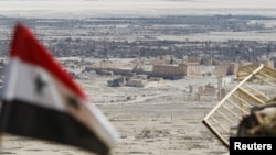 FILE - A Syrian national flag flutters as the ruins of the historic city of Palmyra are seen in the background, in Homs Governorate, Syria, April 1, 2016. 