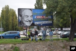 FILE - Activists from the Egyutt (Together) opposition party stand in front of billboards of the government's campaign against George Soros and his support for migration in Budapest, Oct. 5, 2017.