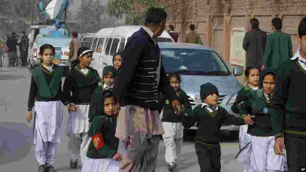 A plainclothes security officer escorts students rescued from nearby school during a Taliban attack in Peshawar, Pakistan, Tuesday, Dec. 16, 2014. 