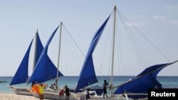 FILE - Tourists takes photographs along local sailboats on the island of Boracay, central Philippines, Jan. 18, 2016. 