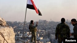 A Syrian government soldier a V-sign under a Syrian national flag as he overlooks eastern Aleppo after troops took control of al-Sakhour neighborhood in Aleppo, Syria, in this handout picture provided by SANA, Nov. 28, 2016.