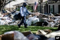 FILE - Postal worker Lonzell Rector makes his rounds among flood-damaged debris from homes that lines the street in the aftermath of Hurricane Harvey in Houston, Sept. 7, 2017.