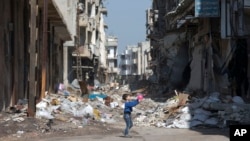 Seorang anak Suriah bermain di antara reruntuhan gedung di kota Homs, Suriah (26/2).