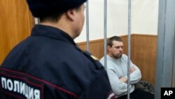 FILE - Former Russian police officer Denis Konovalov, right, sits in a cage prior to a court hearing in Moscow, Russia, Jan. 30, 2020.