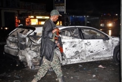 FILE - A Somalia soldier walks past destroyed cars after one of two car bombs, in Mogadishu, Somalia, Aug. 5, 2018.