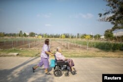 Sampao Jantharun (L), 78, assists Somjit Phuthasiri, 90, on a wheelchair as they head to their home at Wellness Nursing Home Center in Ayutthaya, Thailand, April 9, 2016.