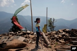In this April 8, 2016 photo, Khendo Tamang, 8, stands near the debris of the collapsed home she was trapped in after the April 25, 2015 earthquake struck in Banskharka, Nepal.