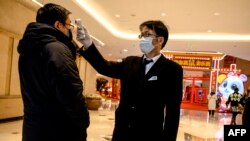 Seorang petugas keamanan memeriksa suhu seorang pengunjung di sebuah pusat perbelanjaan di Shanghai, 8 Februari 2020.