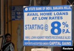 FILE - A woman stands near a bank advertisement for home loans outside a bank in the southern Indian city of Hyderabad, March 22, 2010. Traditional home loans are not available to the hundreds of millions of informal workers who make up the bulk of India's labor force. The creation of micro home finance companies has changed that.