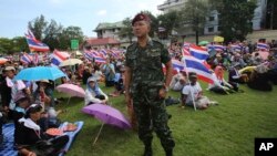 A Thai soldier stands as anti-government protesters sit at the Royal Thai Army compound in Bangkok, Thailand, Friday, Nov. 29, 2013.