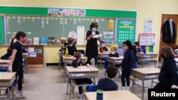 FILE - A teacher calls names for schoolchildren to collect a swab and test themselves for COVID-19 to prevent the spread of the coronavirus disease (COVID-19) in the classroom at South Boston Catholic Academy in Boston, Massachusetts, Jan. 28, 2021. 