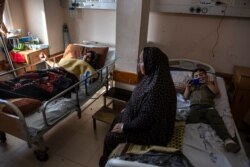 Ihsan Al-Masri, 24, left, rests at the Shifa hospital in Gaza City, May 13, 2021, as her son plays on a mobile phone on the bed next to her. She was injured in a May 10 Israeli strike that hit a near her home.