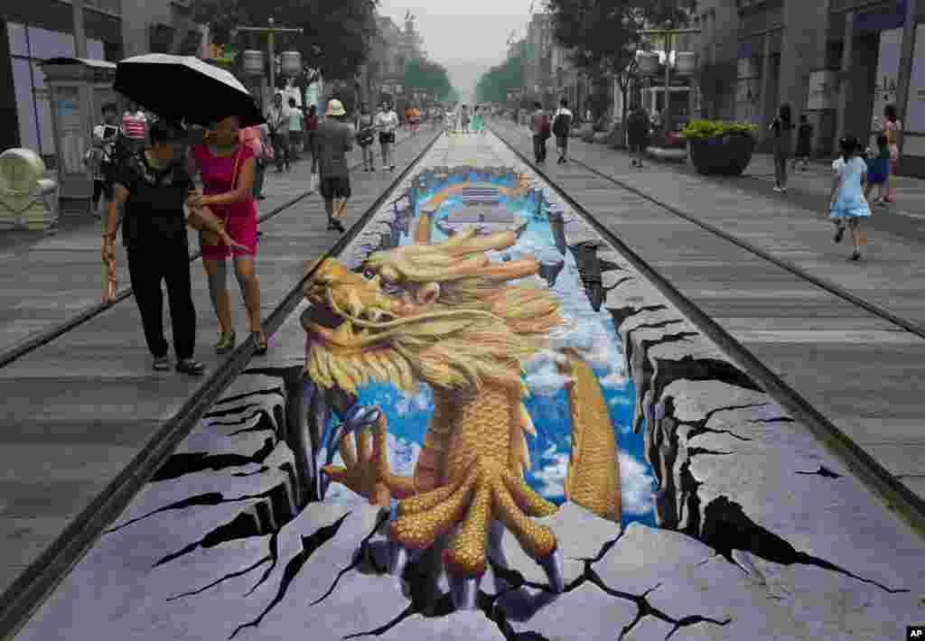 Seorang perempuan China menyaksikan lukisan naga tiga dimensi di jalanan Qianmen, salah satu tempat wisata terpopuler di Beijing, China (11/8). 