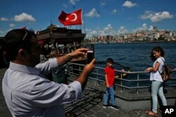 FILE - Tourists take pictures by the Golden Horn, leading to the Bosporus Strait, in Istanbul, Turkey, Aug. 20, 2018.