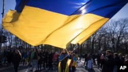 Seorang perempuan mengibarkan bendera Ukraina raksasa dalam protes memperingati dua tahun invasi besar-besaran Rusia, di Gerbang Brandenburg, Berlin, Sabtu, 24 Februari 2024. (Foto: AP)