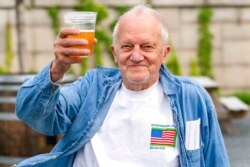 FILE - George Ripley, 72, of Washington holds up his free beer after receiving the J &amp; J COVID-19 vaccine shot, at The REACH at the Kennedy Center in the nation's capital, May 6, 2021.