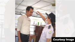 មន្ត្រីសុខាភិបាលប្រចាំនាយកដ្ឋានប្រយុទ្ធនឹងជំងឺឆ្លង CDC កំពុងពិនិត្យសីតុណ្ហភាពបុរសម្នាក់។ យោងតាមក្រសួងសុខាភិបាលកម្ពុជា​ មនុស្សជាង ១ពាន់នាក់​ត្រូវបានធ្វើតេស្តរកវីរុសកូរ៉ូណា ឬកូវីដ-១៩។ (រូបថតដោយនាយកដ្ឋានប្រយុទ្ធនឹងជំងឺឆ្លង CDC)