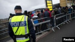 FILE - A police officer keeps guard as migrants arrive at Hyllie station outside Malmo, Sweden. Picture taken Nov. 19, 2015. 