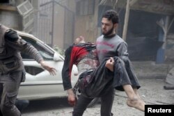 In the Syrian town of Douma, a resident carries an injured man past a damaged site, Oct. 29, 2015. Activists said Assad loyalists bombed a field hospital there.