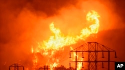 FILE - Flames burn near power lines in Sycamore Canyon near West Mountain Drive in Montecito, Calif., Dec. 16, 2017. As California counties face power shutoffs meant to prevent wildfires, counties with more resources are adapting easier than poorer ones.