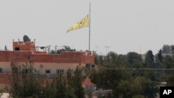 In this photo taken from the Turkish side of the border between Turkey and Syria, in Akcakale, southeastern Turkey, a flag of the Kurdish People's Protection Units, or YPG, flies over the town of Tal Abyad, Syria, June 16, 2015. 