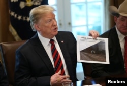 FILE - President Donald Trump holds up a photo of a "Typical Standard Wall Design" as he hosts a discussion on border security and safe communities with state, local, and community leaders in the Cabinet Room of the White House in Washington, Jan. 11, 2019.