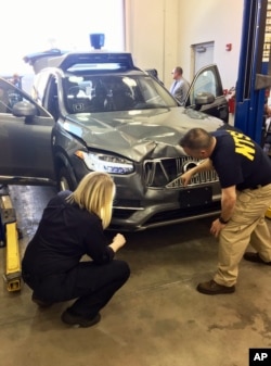 In this March 20, 2018, photo provided by the National Transportation Safety Board, investigators examine a driverless Uber SUV that fatally struck a woman in Tempe, Ariz. (National Transportation Safety Board via AP)