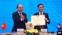 Vietnamese Prime Minister Nguyen Xuan Phuc, left, applauds as Minister of Trade Tran Tuan Anh, right, holds up a signed document during a virtual signing ceremony of the Regional Comprehensive Economic Partnership, or RCEP, trade agreement in Hanoi.