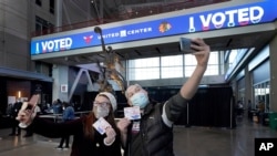 នាង Samantha Jones, ឆ្វេង និង​លោក Peter Vina ថតរូប​ស៊ែលហ្វី នៅ​ជិត​រូបសំណាក​របស់​លោក Michael Jordan នៅ​ថ្ងៃបោះឆ្នោត កាលពី​ថ្ងៃអង្គារ ទី៣ ខែវិច្ឆិកា ឆ្នាំ២០២០ នៅឯ​មណ្ឌល​បោះឆ្នោត​មួយ​កន្លែង នៅក្នុង​ទីក្រុង Chicago។