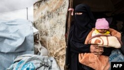Seorang perempuan Suriah menggendong bayi sambil mengemas barang-barang pribadi sebelum meninggalkan kamp Al Hol yang dikelola oleh Kurdi, di al-Hasakeh, Suriah, Senin, 16 November 2020. 