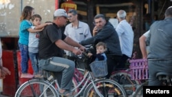 Syrian children ride a bicycle with their father at the main market at the Al-Zaatari refugee camp in Mafraq, Jordan, June 1, 2017. 