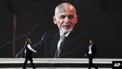 Men walk past a mural of President Ashraf Ghani at Hamid Karzai International Airport, in Kabul, Afghanistan, Aug. 14, 2021.