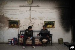 FILE - Two men sit in their burned house as they returned home after the neighborhood was retaken by Iraqi security forces from Islamic State militants, on the western side of Mosul, Iraq, March 29, 2017.