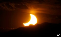 FILE - The annular solar eclipse is seen as the sun sets behind the Rocky Mountains from downtown Denver, Colorado, May 20, 2012.