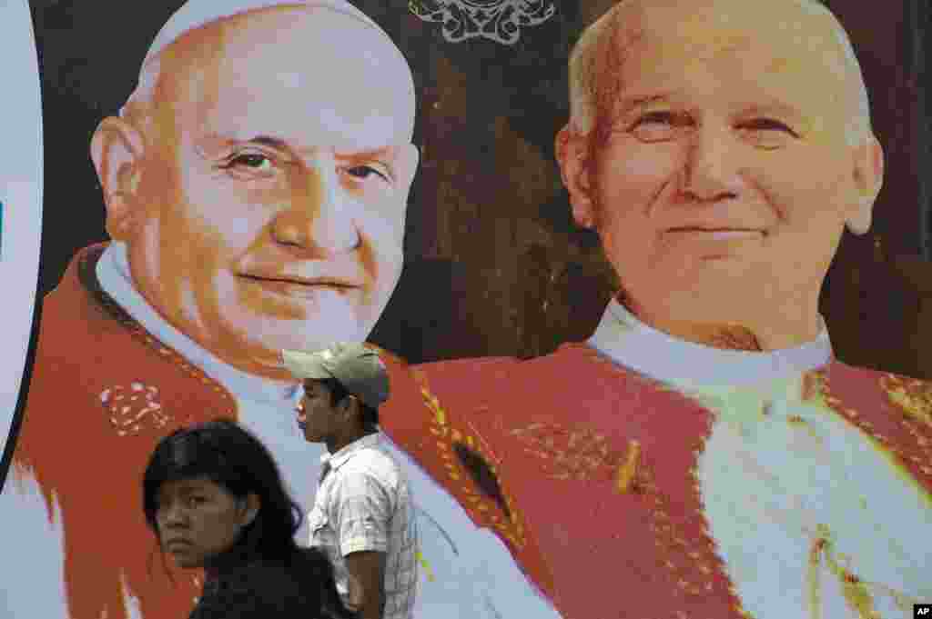 Two people walk in front of images of Pope John XXIII, left, and Pope John Paul II, Guatemala City, April 27, 2014.