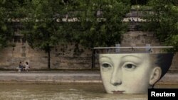 People hang out by the River Seine near an art installation for the Olympics, in Paris, France, August 3, 2024. 