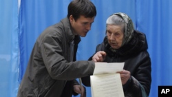 A young man helps an elderly voter read her voting ballot at a polling station in Kiev, Ukraine, Sunday, Oct. 28, 2012.
