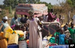 FILE - Refugees who fled the recent violence in South Sudan and crossed the border into Uganda carry their belongings as they await transportation from a transit center in the town of Koboko to a nearby settlement in Arua District, in northern Uganda, Jan. 6, 2014.