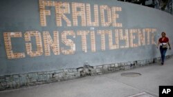 FILE - A pedestrian walks next to a message on a wall formed with Venezuelan currency that reads in Spanish: “The Constituent Assembly is a fraud” in Caracas, Venezuela, July 31, 2017.