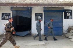 FILE - Afghan police walk past Islamic State flags on a wall, after an operation in the Kot district of Jalalabad province east of Kabul, Afghanistan, Aug. 1, 2016.