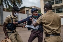 FILE - A demonstrator is arrested by Ugandan police officers at a protest for more food distribution by the government to people who have been struggling during the nationwide lockdown imposed to curb the spread of the COVID-19, in Kampala, May 18, 2020.