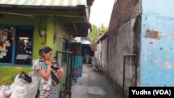 Istri Pamuji, Hartini, menggendong anaknya yang berusia satu setengah tahun di pintu gang menuju rumahnya di Cengklik Nusukan Solo. (Foto: VOA/Yudha)