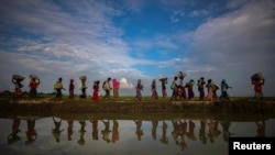 Rohingya refugees are reflected in rain water along an embankment next to paddy fields after fleeing from Myanmar into Palang Khali, near Cox's Bazar, Bangladesh November 2, 2017. REUTERS/Hannah McKay