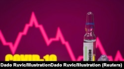A test tube labelled with the Vaccine is seen in front of Covid-19 and stock graph logo in this illustration taken