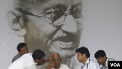 Tim dokter memeriksa aktivis Anna Hazare di depan potret raksasa Mahatma Gandhi, Selasa (23/8).